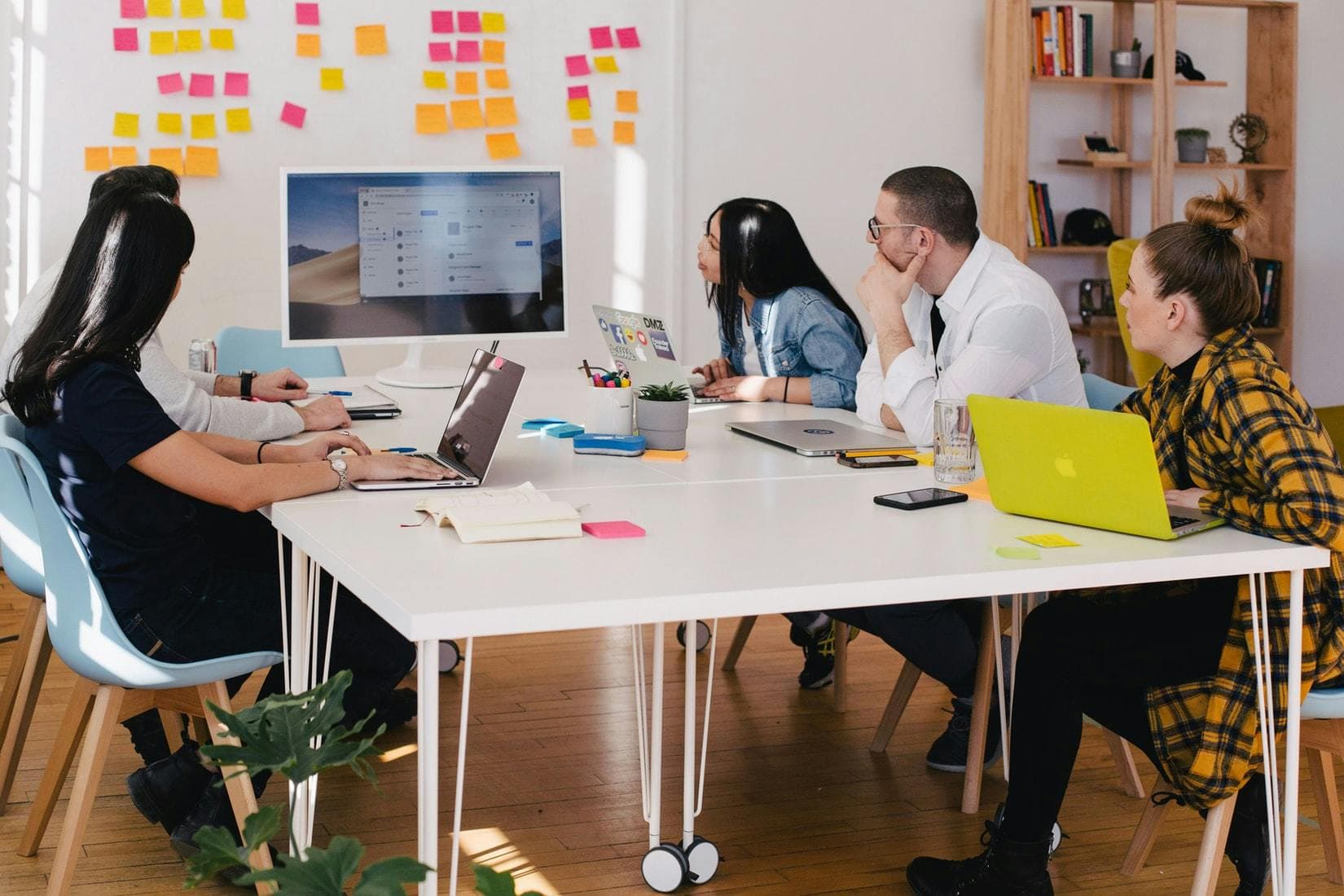 people sitting around a white table in a boardroom looking at a computer screen