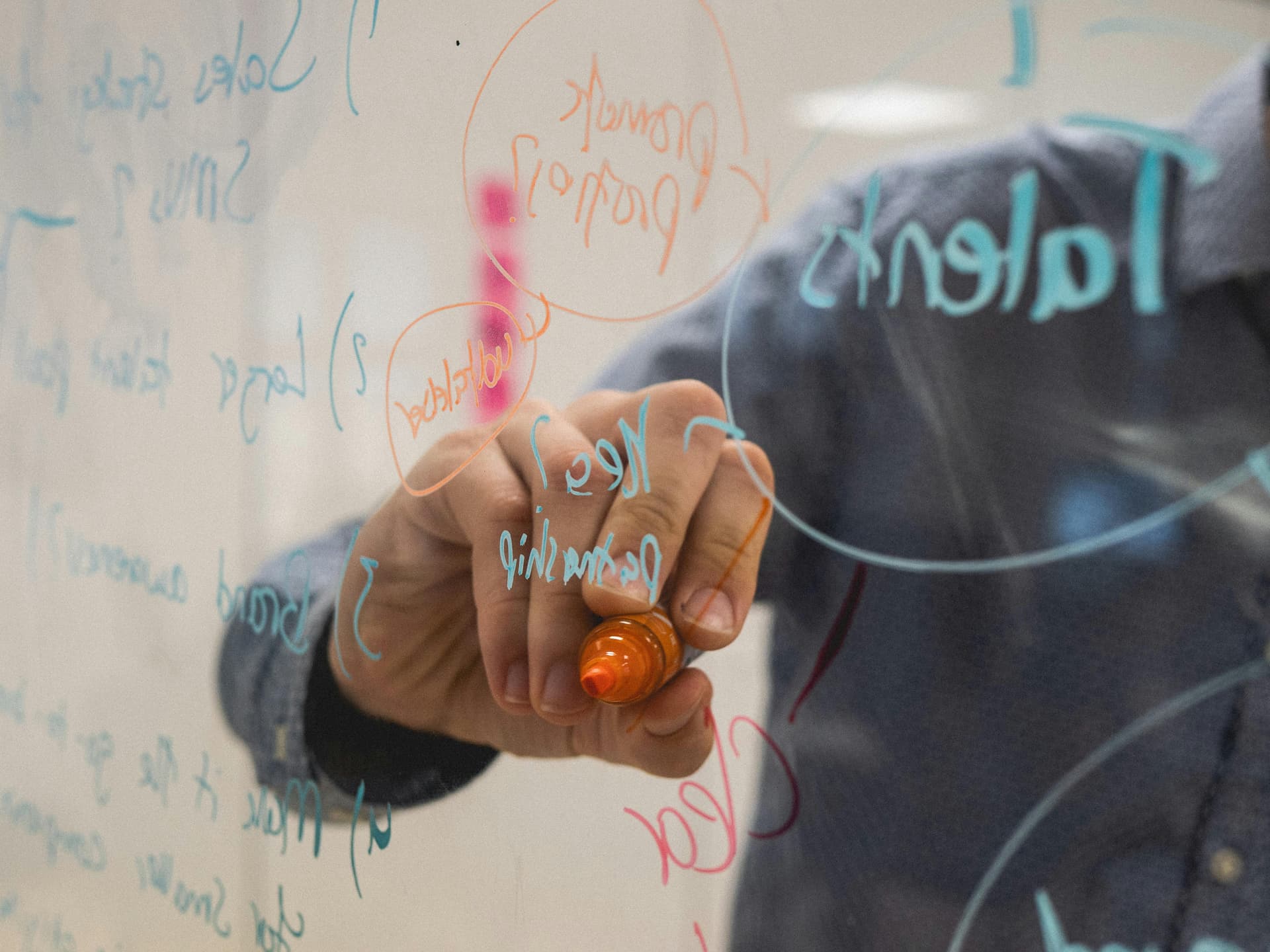 Person writing on a clear whiteboard, jotting down ideas. 