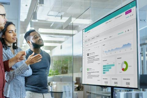 Three people look at a Meltwater dashboard on a large monitor screen for a blog about trend forecasting.