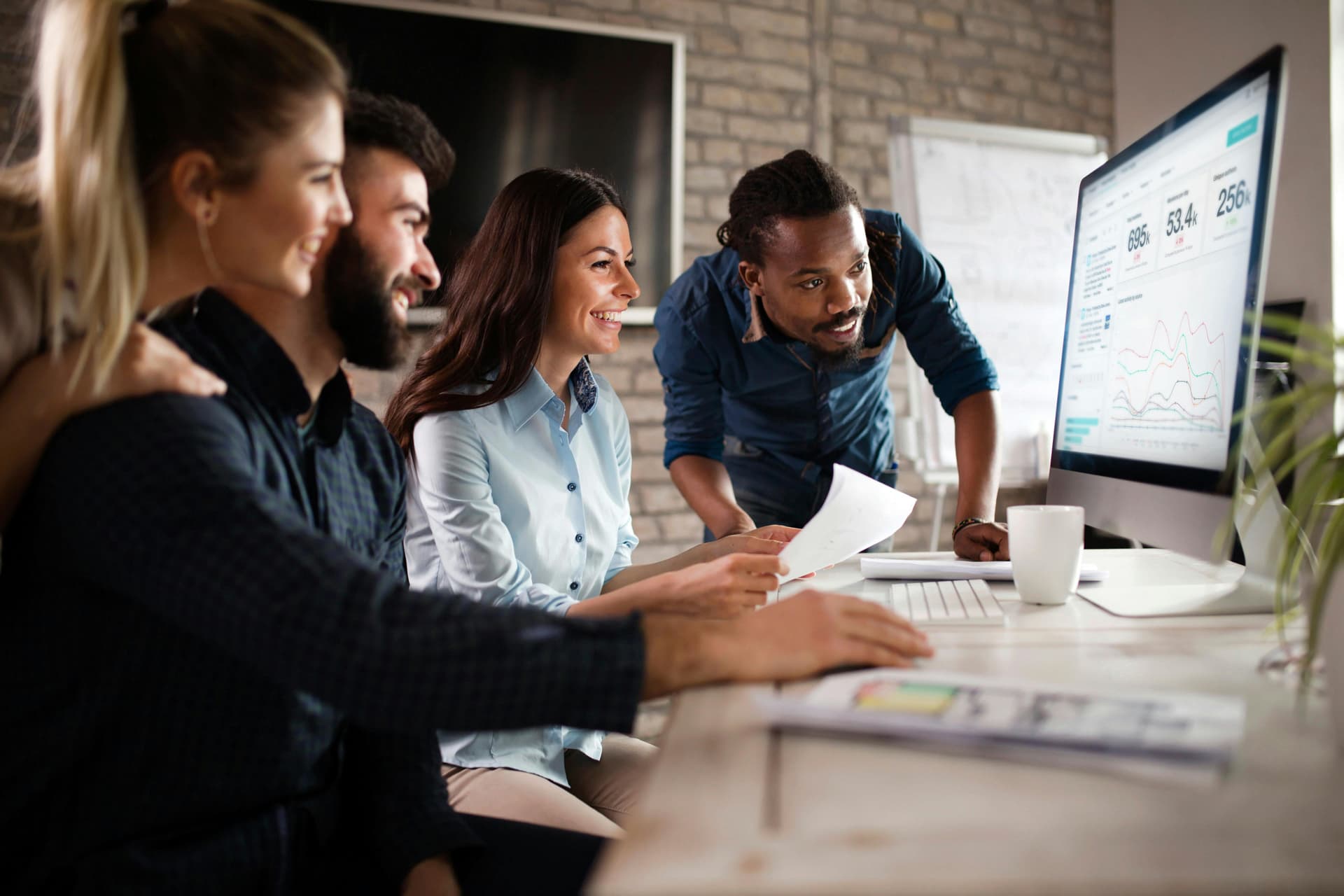 A photo of a group of smiling people gathered around a desktop computer logged into the Meltwater platform for a guide to trend detection algorithms.