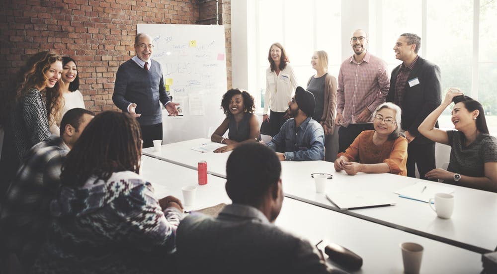 People sitting around a table whule a pan stands infront of a whiteboarding presenting