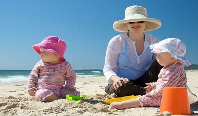 Two babies playing on the beach with their mum.