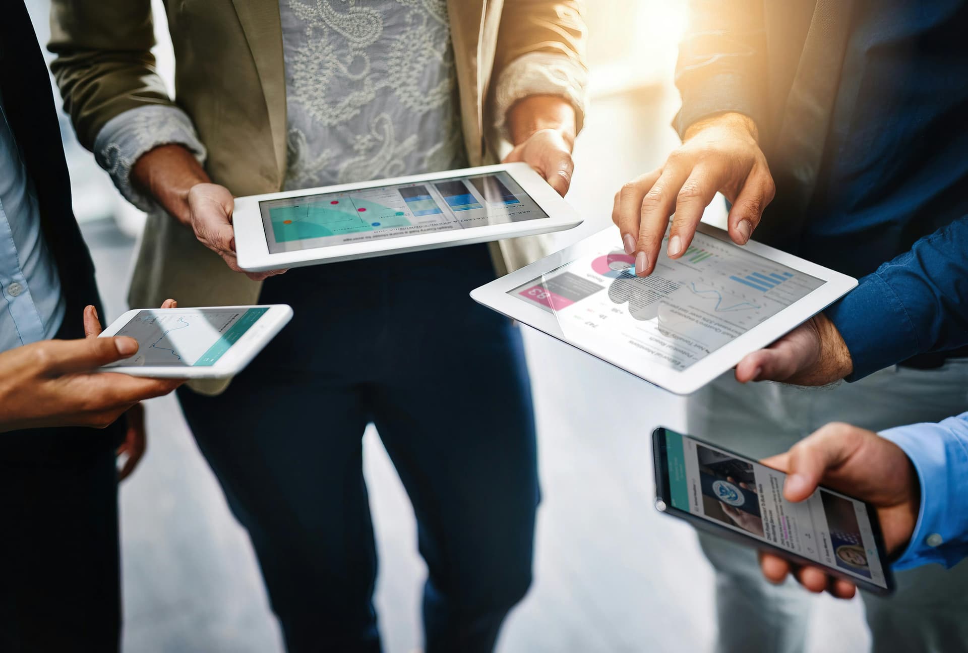 A photo four people gathered together, holding their tablets and mobile phones and accessing the Meltwater platform for this guide to trend detection and trend detection algorithms.