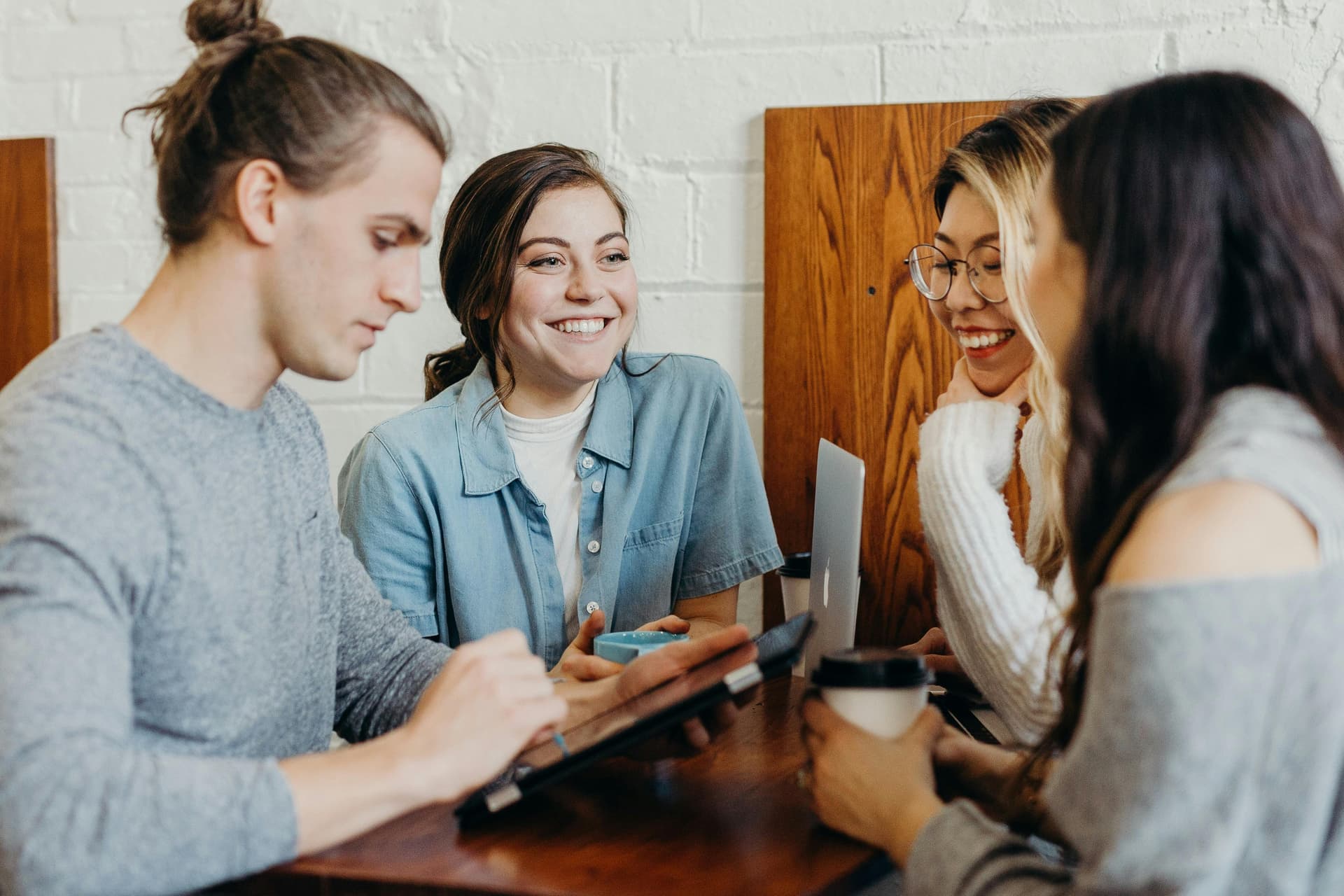 Group of diverse people at a table in a coffee shot looking at tablets and phones