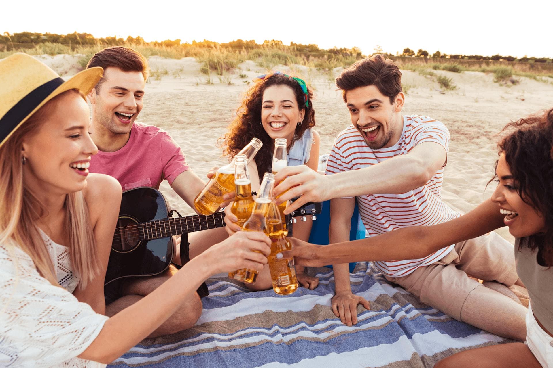 group of people gathers on a beach toasting with bottles of beer