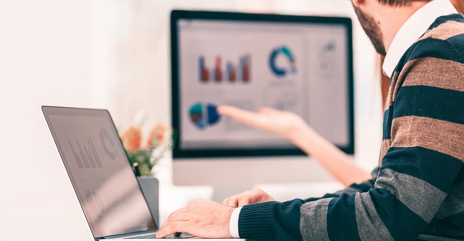 Image of a man sitting at a laptop with a screen showing graphs 