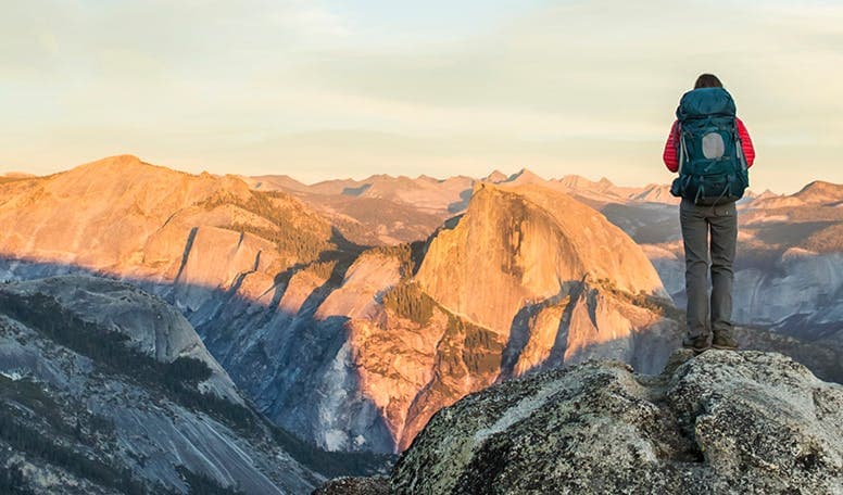 Man hiking and standing on top of a mountain with a back pack.