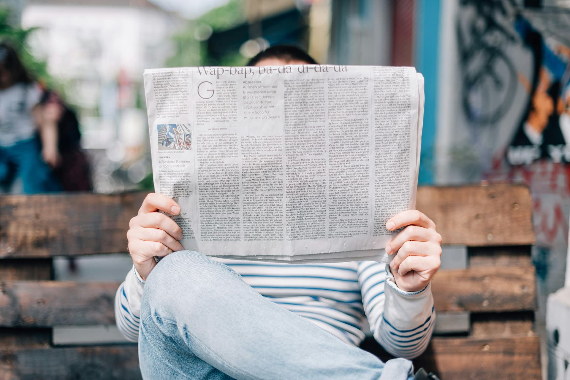 Person on park bench reaching a newspaper. Tips for pitching a press release and getting reporters to pick up your new story
