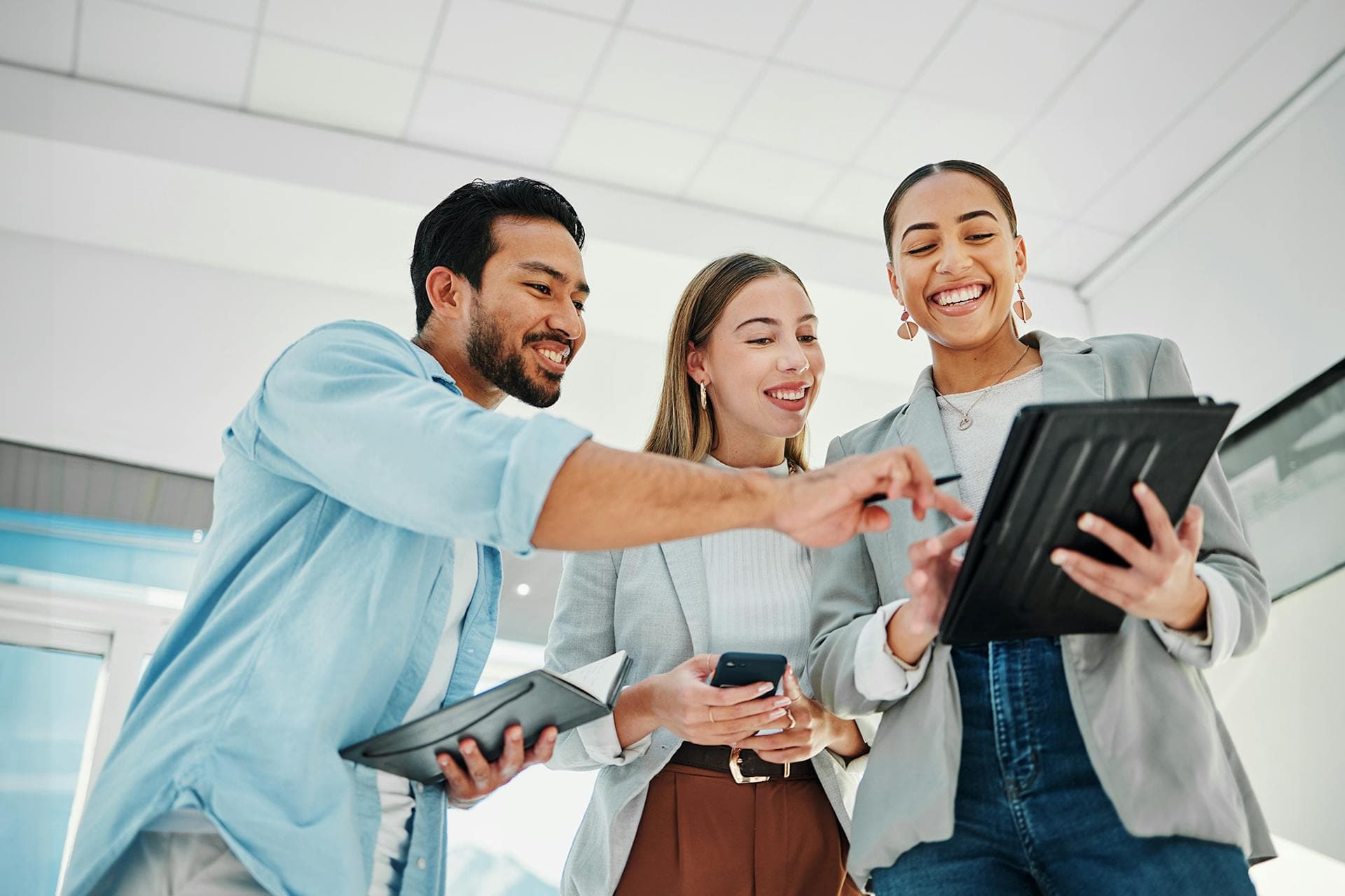 A group of happy social media marketers  in an office looking and pointing at a tablet.