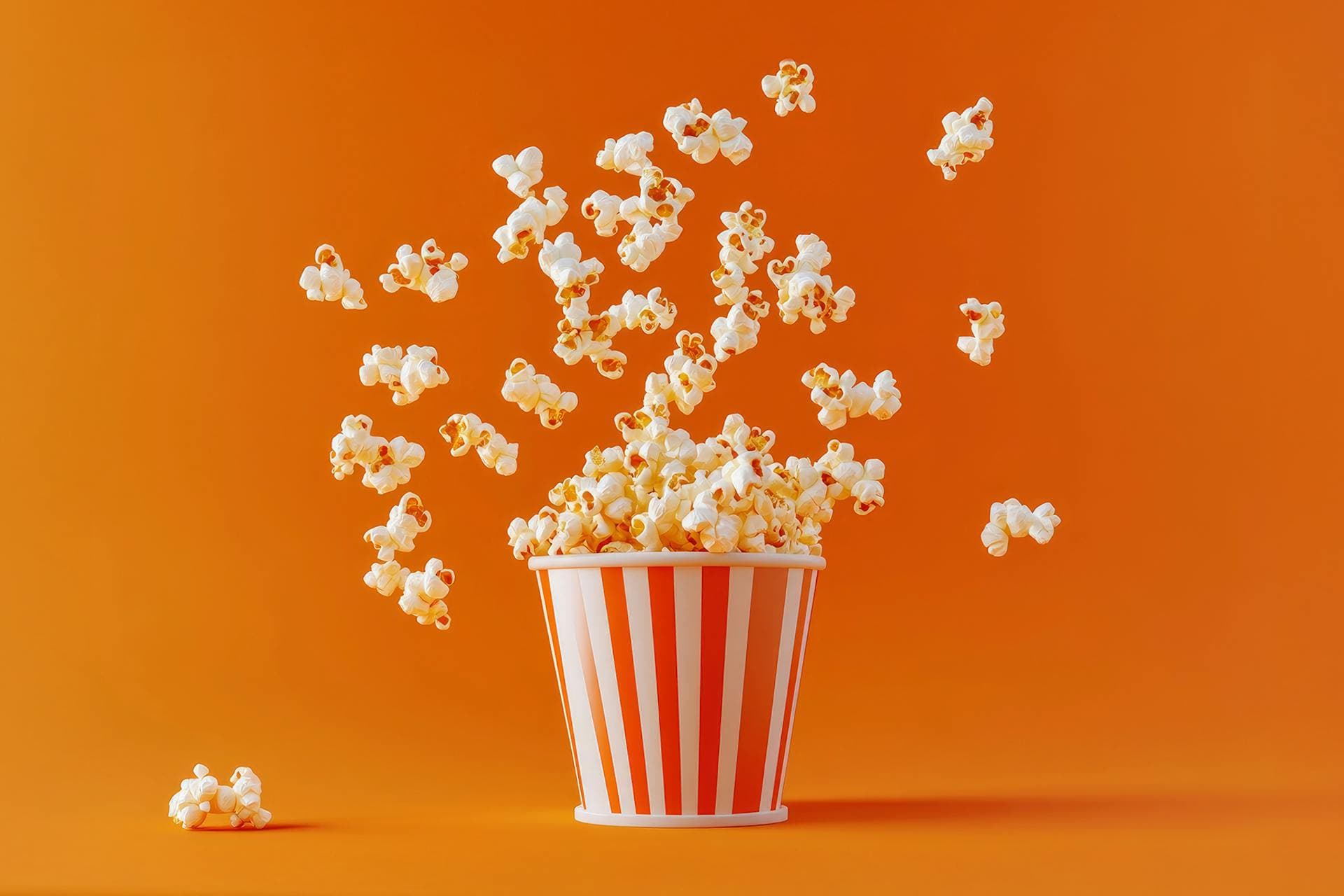 Popcorn exploding out of a red and white striped movie theater popcorn bucket 