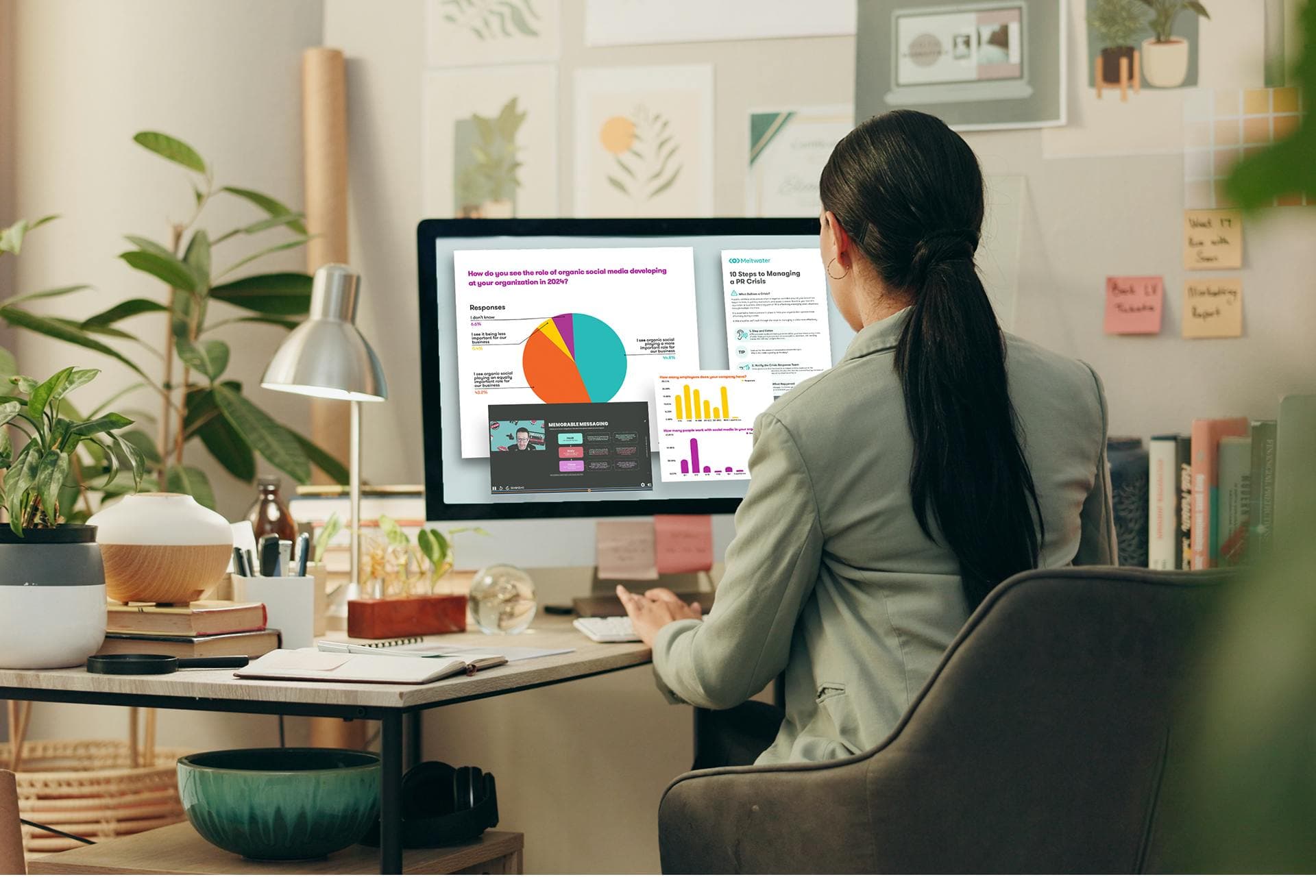 Bild einer Social-Media-Managerin, die an ihrem Schreibtisch vor einem großen Desktop-Computer sitzt. Der Computer zeigt verschiedene Diagramme und Ressourcen für Social-Media-Manager. Social Media Toolkit herunterladen.