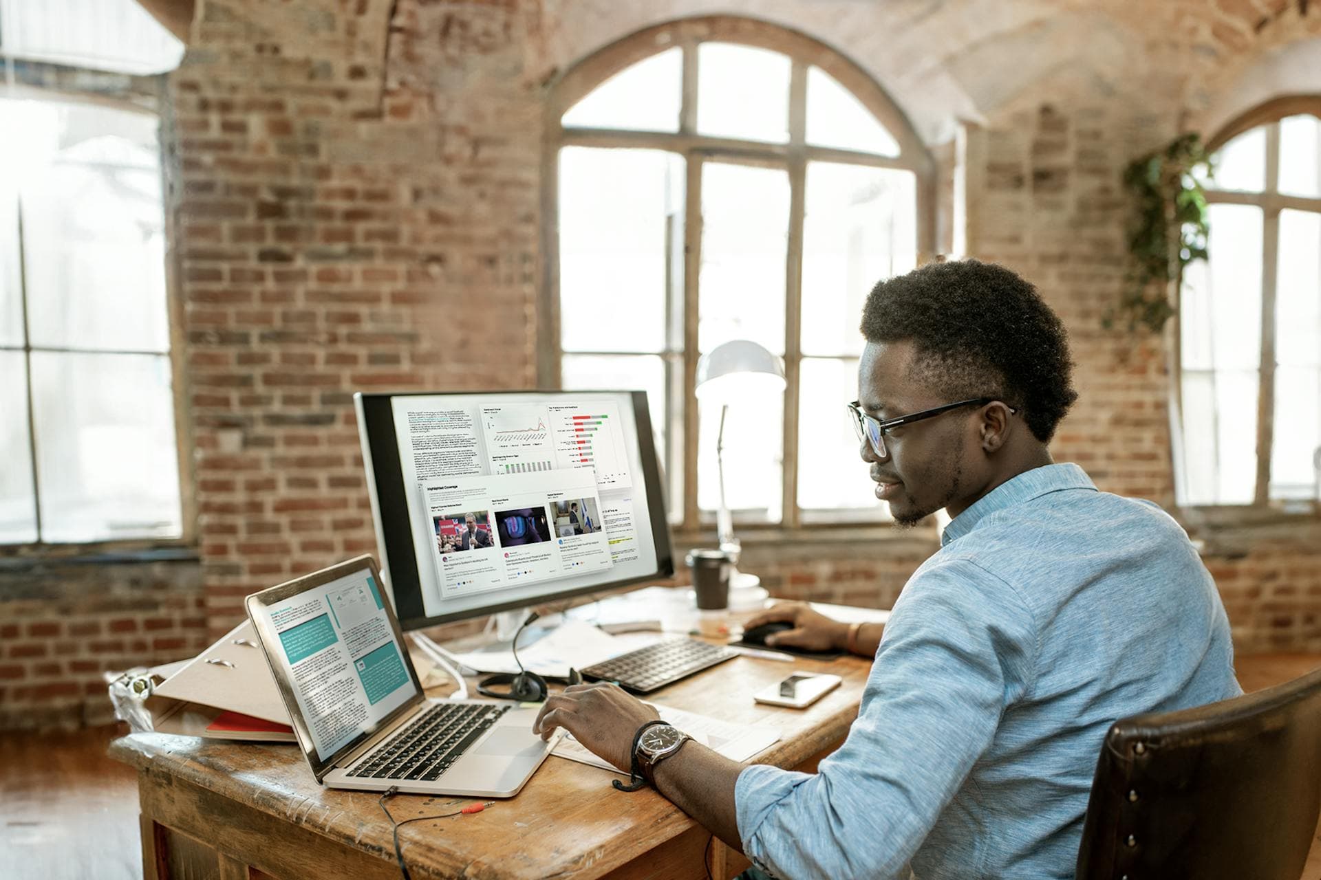 Bild eines PR-Fachmanns, der an seinem Schreibtisch vor einem großen Monitor und einem Laptop sitzt. Die Computer zeigen verschiedene Diagramme und Tools für PR-Fachleute. PR-Toolkit herunterladen